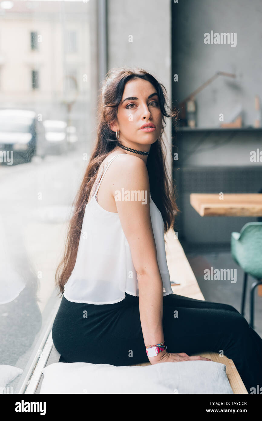 Porträt der jungen kaukasischen Frau sitzt auf der Bank und suchen Kamera in helle Wohnung - Jugend, neue Generation, fröhlich Stockfoto
