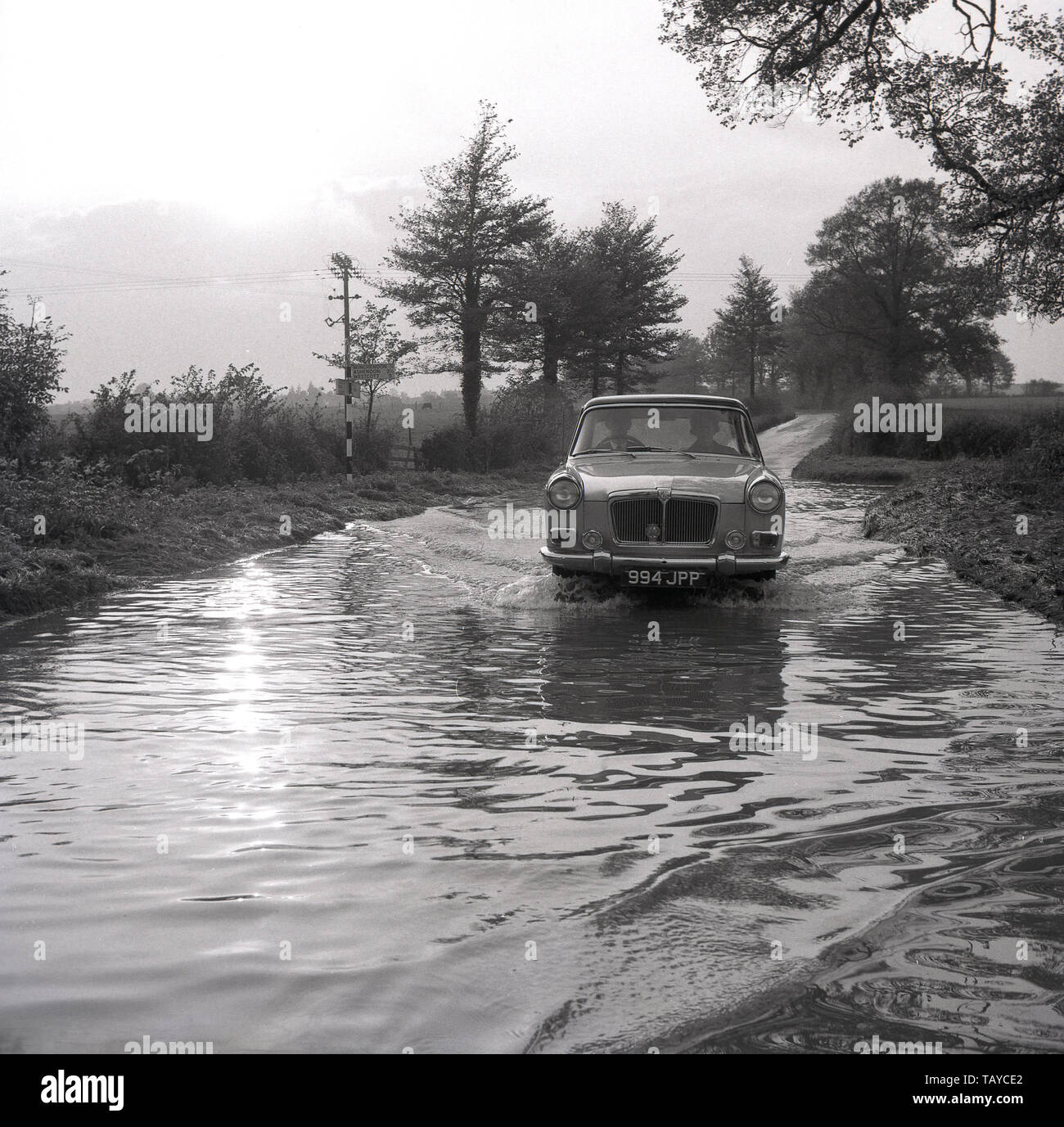 1960, historische, ein MG Auto durch das Wasser auf einem überfluteten Landstraße, Buckinghamshire, England, Großbritannien fahren. Stockfoto