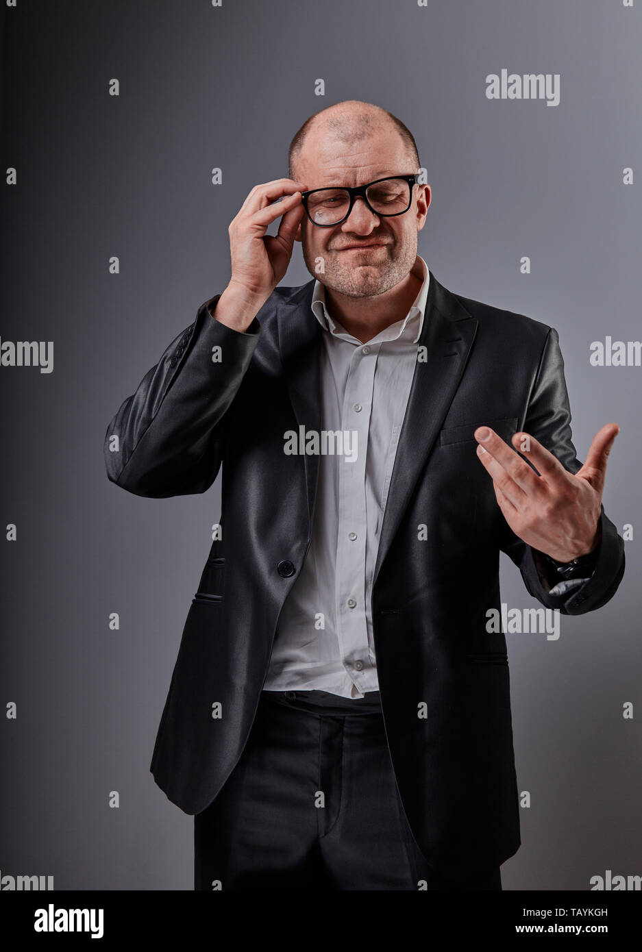 Unglücklich deprimiert gestikulierend busuness Mann im schwarzen Anzug und Brille Grimassen auf grauem Hintergrund. Closeup Portrait Stockfoto