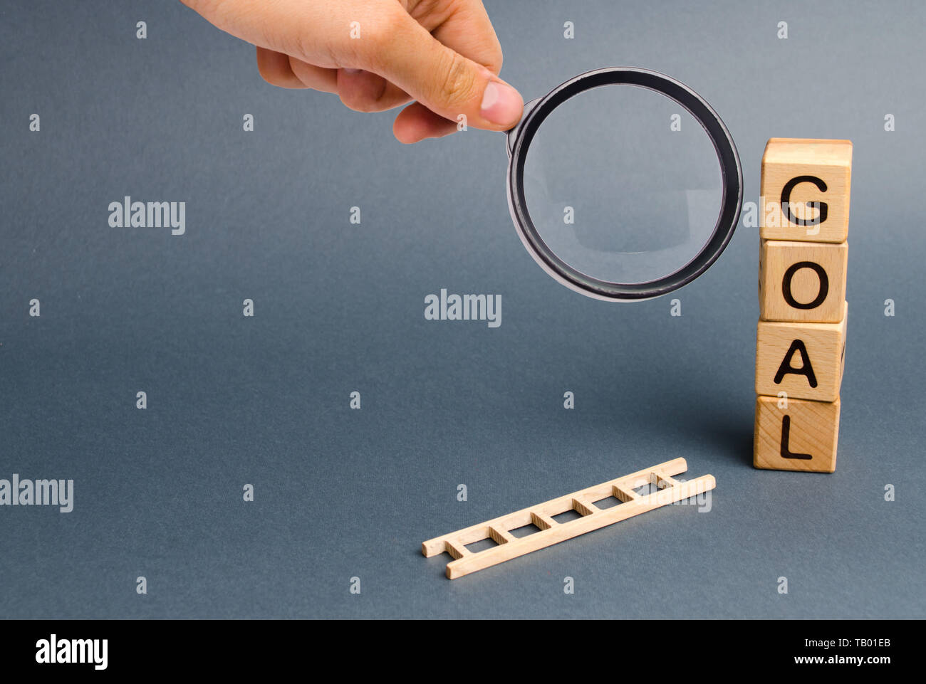 Lupe betrachtet einen Turm aus Würfeln mit einer Inschrift Ziel und einem gefallenen Leiter. Werkzeug für den Erfolg. Geben Sie nicht auf halbem Weg. Stockfoto