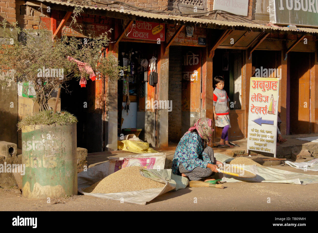 Frau worfeln Reis vor der Straße Geschäfte in der Altstadt von Dhulikhel, Nepal Stockfoto