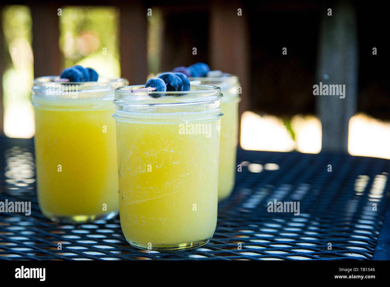 3 Mimosas in Mason Gläser mit blaubeere Spieß garnieren, auf Terrasse Tisch. Stockfoto