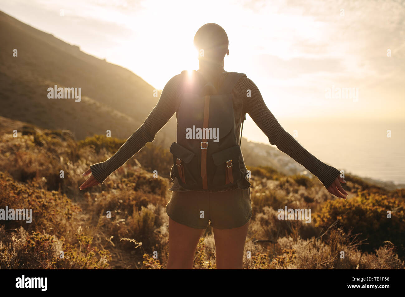 Ansicht der Rückseite Frau mit Rucksack auf Land weg an der Sonne mit ihren Hände ausgestreckt. Weibliche Wanderer Umarmung der Sonne Licht. Stockfoto