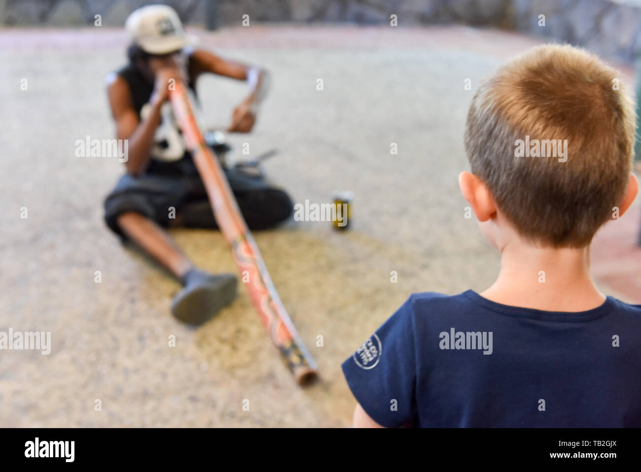 Kaukasische boy watching Aboriginal Mann spielt Musik, Kuranda, Australien Stockfoto