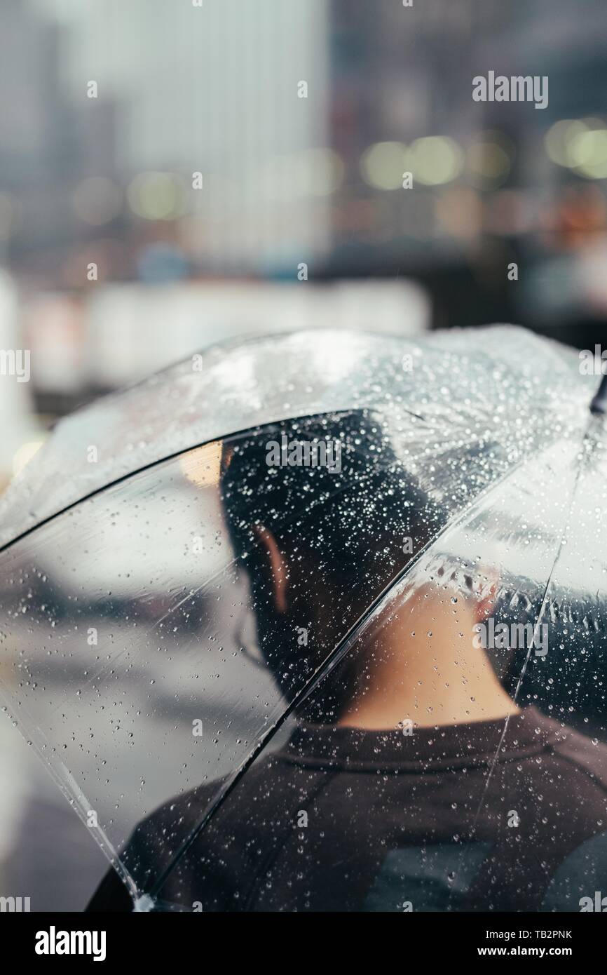 Männlich mit dem Rücken zur Kamera und einem nassen Transparenter Regenschirm, der unter Regen läuft Stockfoto