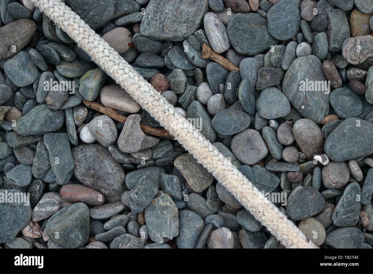 Kieselsteine am Strand mit einigen alten Angeln Seil halten ein Boot aus auf das Meer Stockfoto