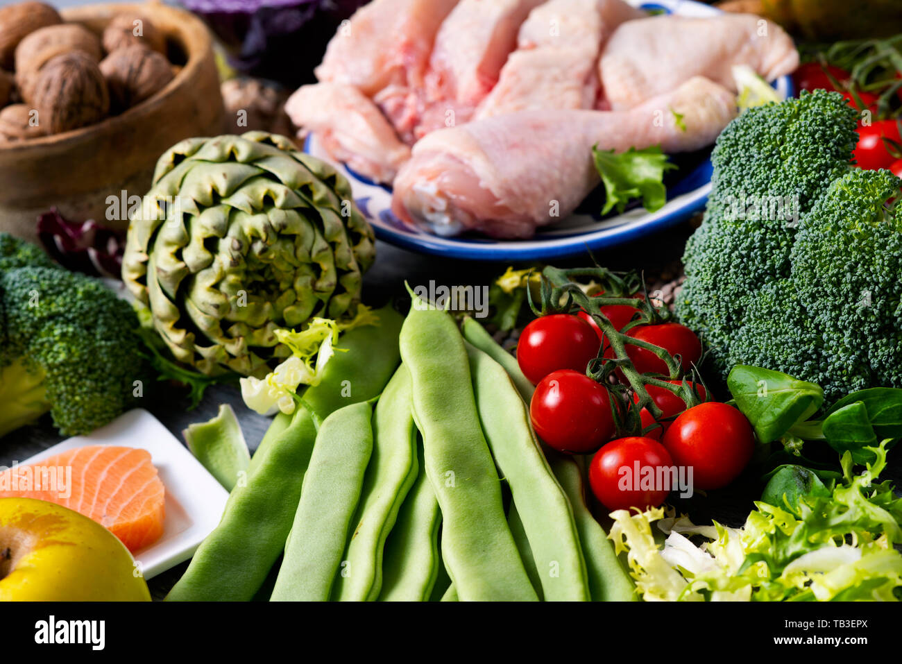 Nahaufnahme von einem Stapel von unverarbeiteten Nahrungsmitteln, wie z. B. verschiedene rohe Früchte und Gemüse, Hülsenfrüchte und Nüsse, einige Stücke von Huhn und Fisch, auf einem Tisch Stockfoto