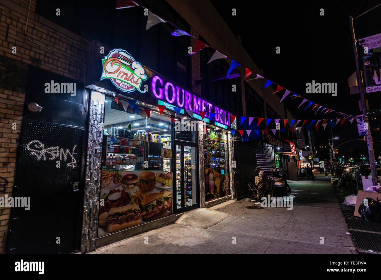 New York City, USA - 31. Juli 2018: Beleuchtetes Display von ein Lebensmittelgeschäft namens Gourmet Deli in der Nacht mit Menschen um in Harlem, Manhattan, New Yo Stockfoto