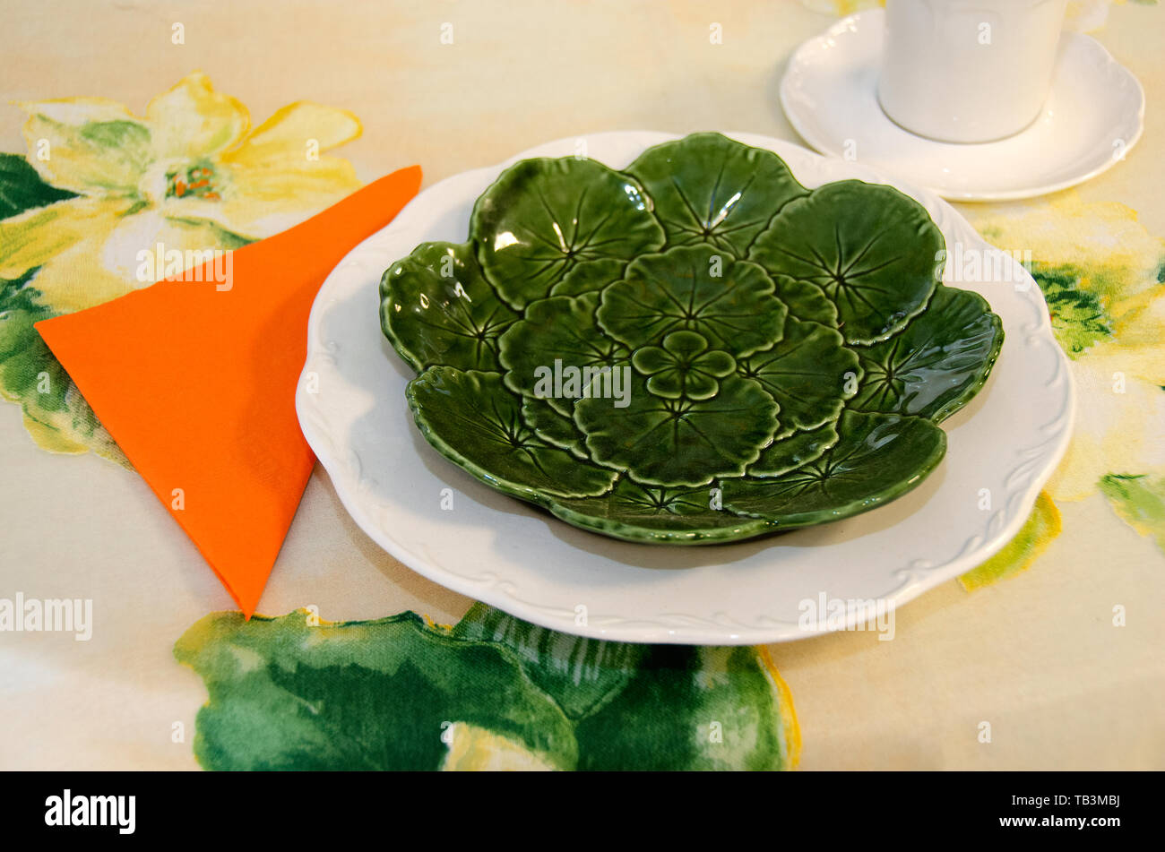 Helle farbige Tabelle Einstellung mit grünem Salatteller und orange Serviette auf blumige Tischdecke Stockfoto