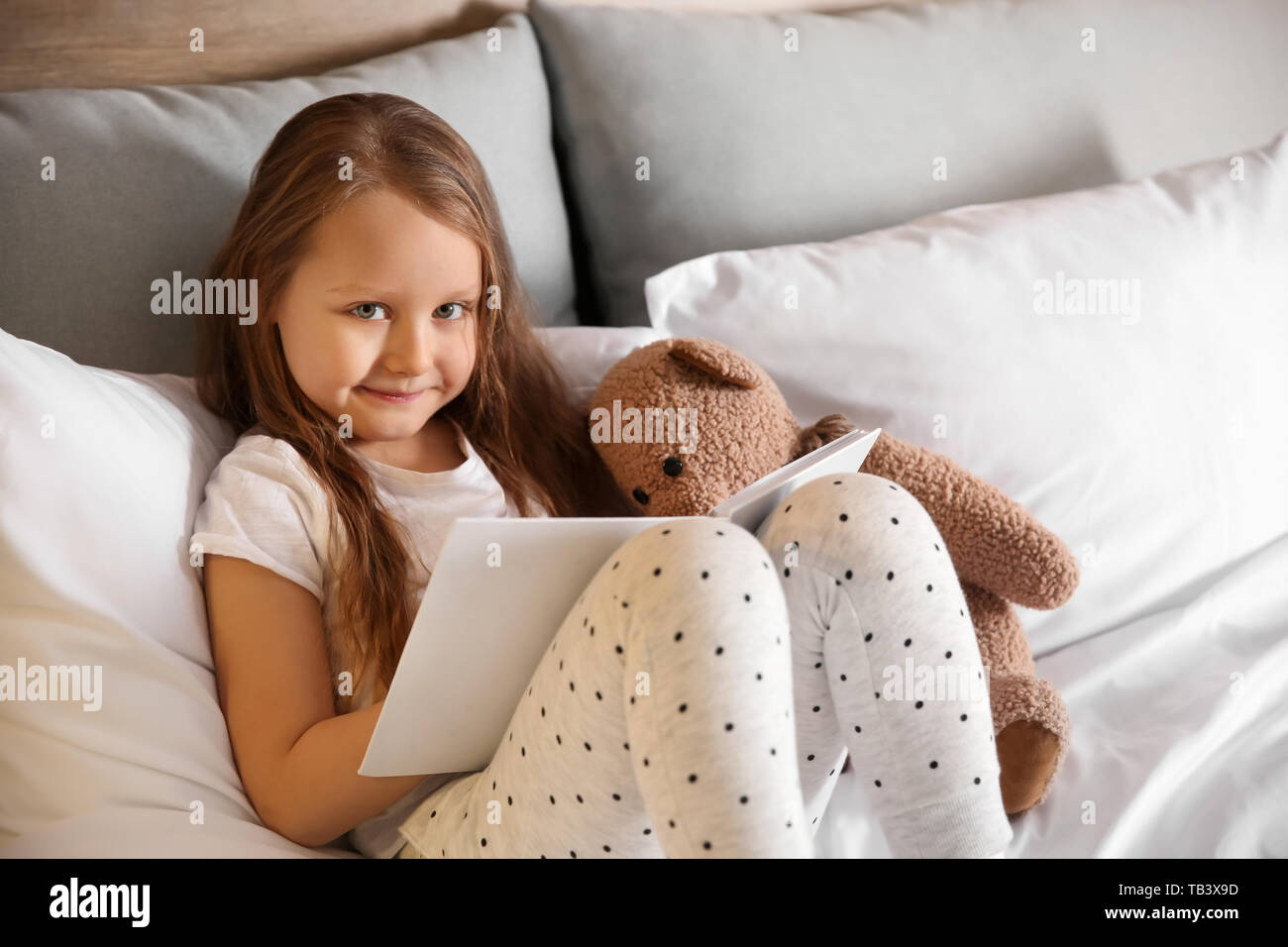 Süße kleine Mädchen mit Spielzeug Bär lesen Buch im Bett Stockfoto
