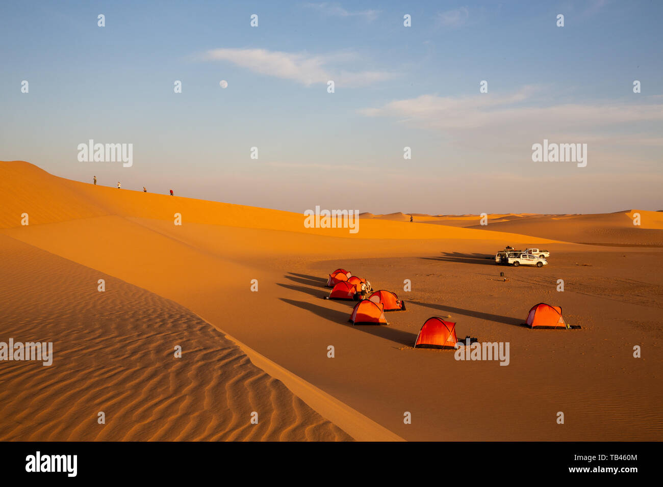 Zelte aufgebaut für wildes Campen in der Abendsonne in der westlichen Wüste des Sudan. Vier Figuren erklimmen Sie den Kamm einer Düne wie der Mond setzt Stockfoto