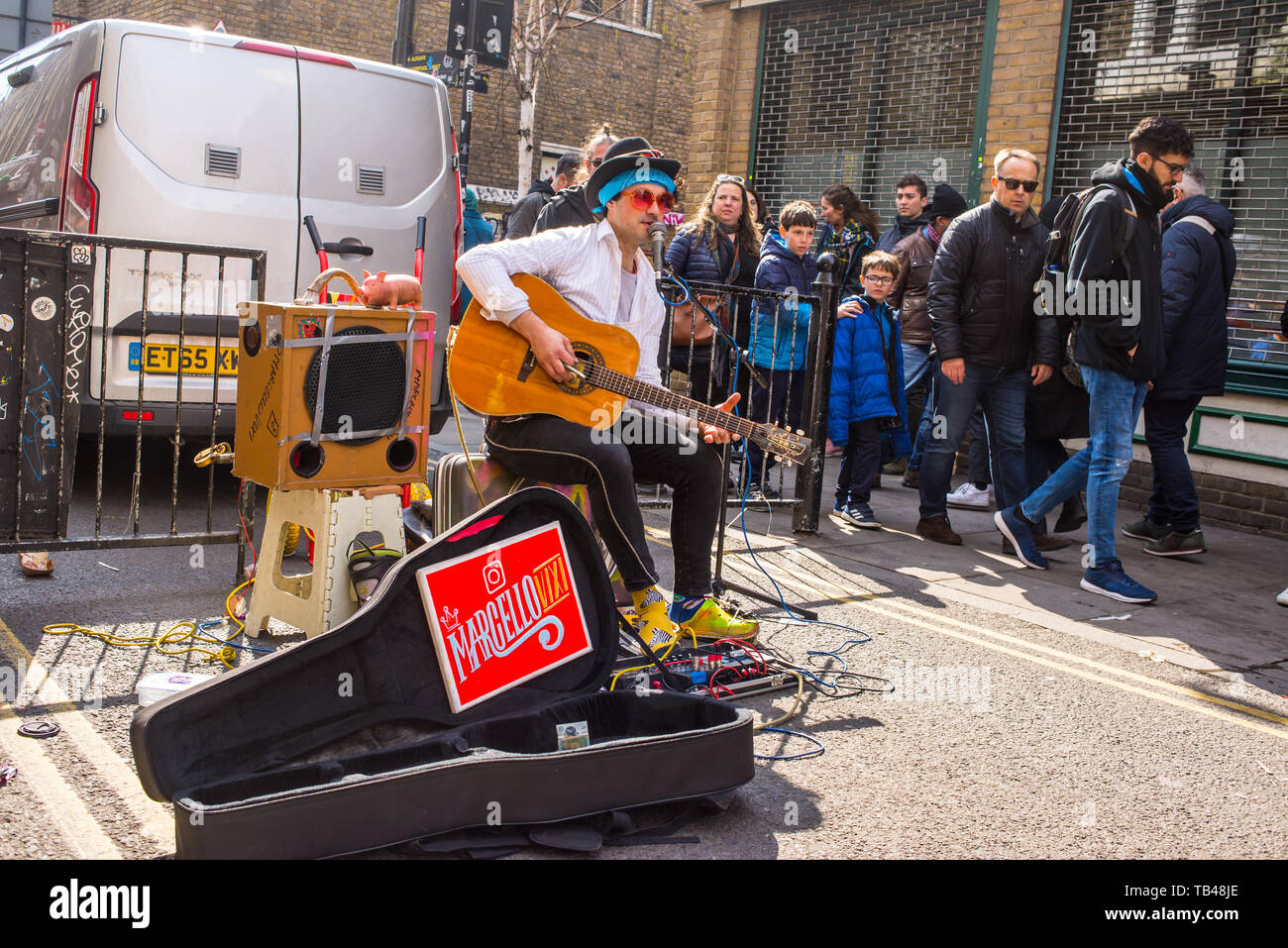 Shoreditch, London, England, UK - April 2019: Junge Gaukler mann straße Musiker Gitarre spielen und singen unter Masse in der Brick Lane, East London Stockfoto