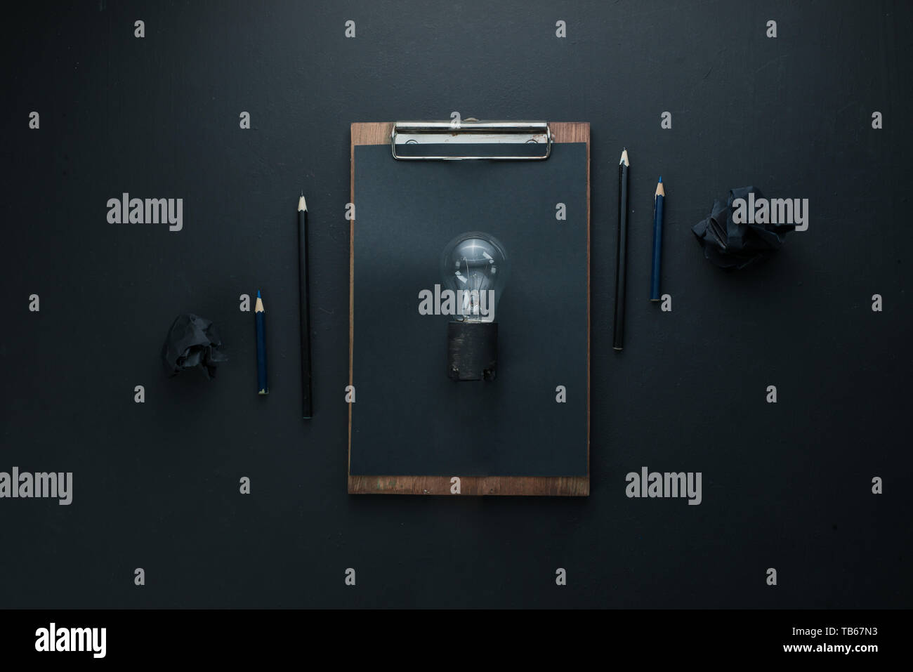 Bau- Konzept, die Glühbirne einer Idee auf einem dunklen Hintergrund mit zerknittertem Papier Kugeln und Stifte. Stockfoto