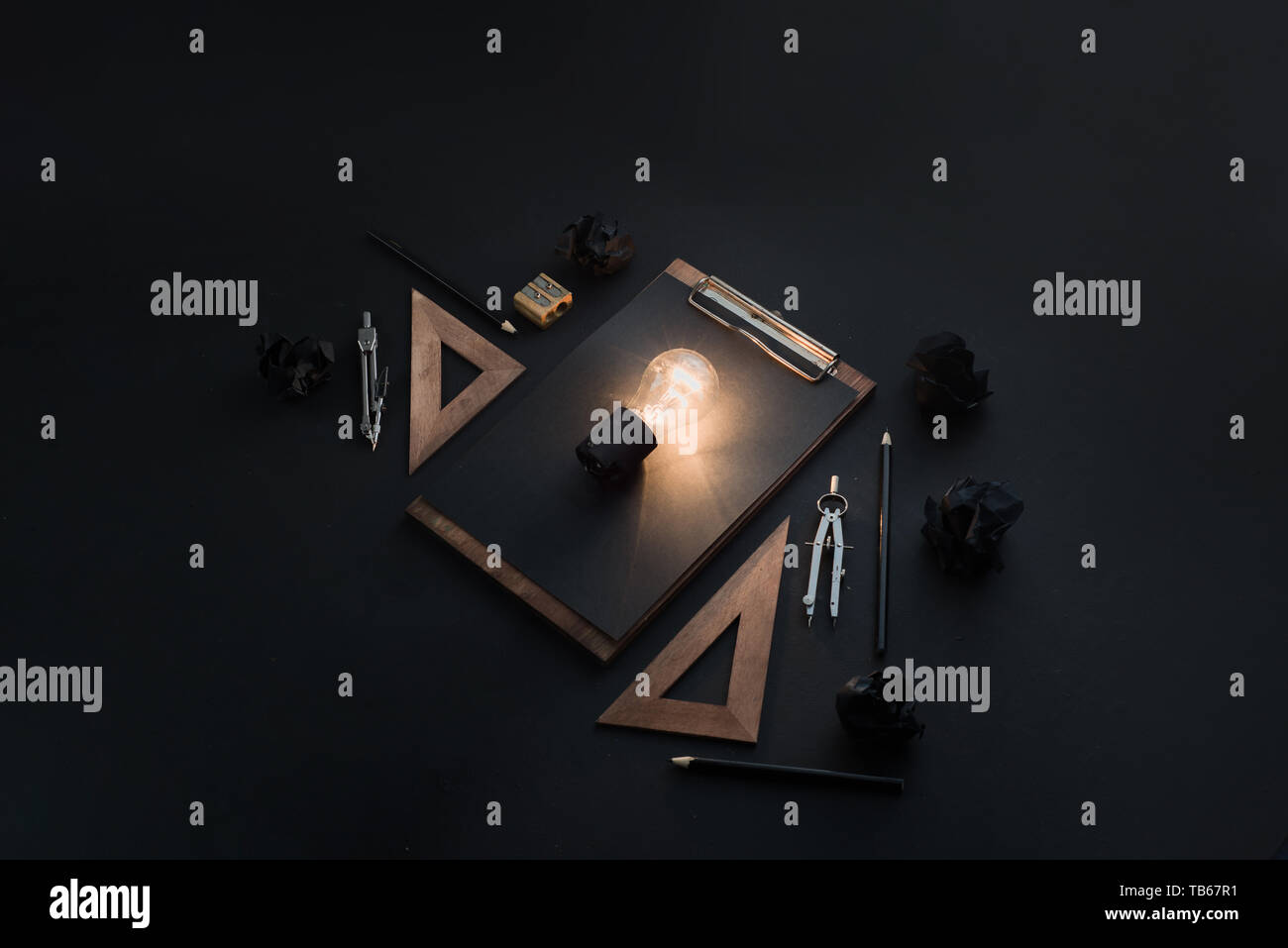Kreative Idee für Konstruktion, Architektur und Konstruktion. Die Glühbirne leuchten in Schwarz auf Schwarz flach mit zerknittertem Papier Kugeln, Lineale, Bleistifte Stockfoto