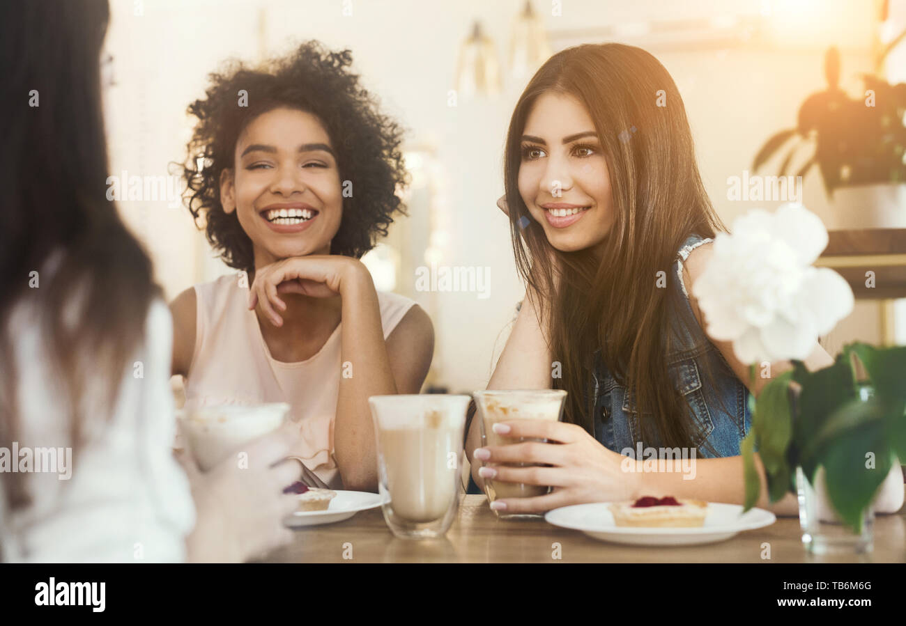 Junge gemischtrassigen Mädchen sitzen im Cafe, Kaffee trinken mit Kuchen und Zuhören lustige Lebensgeschichte von Ihrem Freund Stockfoto