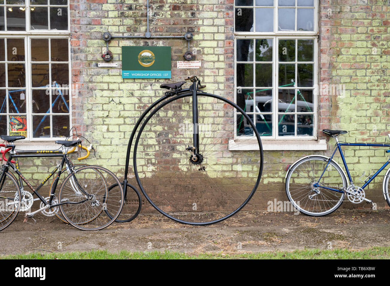 Penny Farthing Fahrrad außerhalb einer Werkstatt im Bicester Heritage Center 'Drive es Tag'. Bicester, Oxfordshire, England Stockfoto
