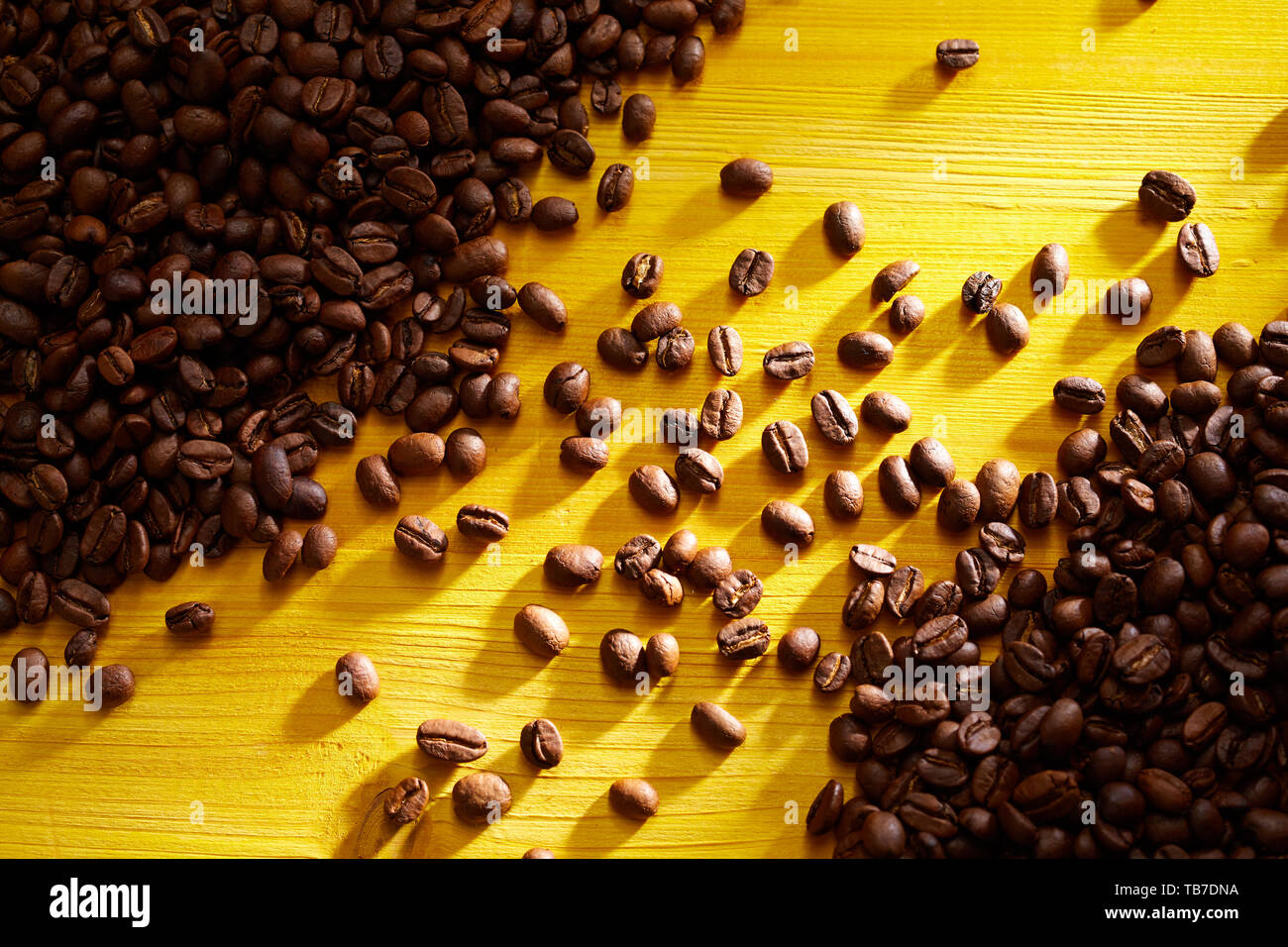 Geröstete Kaffeebohnen in Haufen angeordnet auf zwei gegenüberliegenden Ecken in einer Diagonalen bunt gelb Holz gesehen von oben Stockfoto