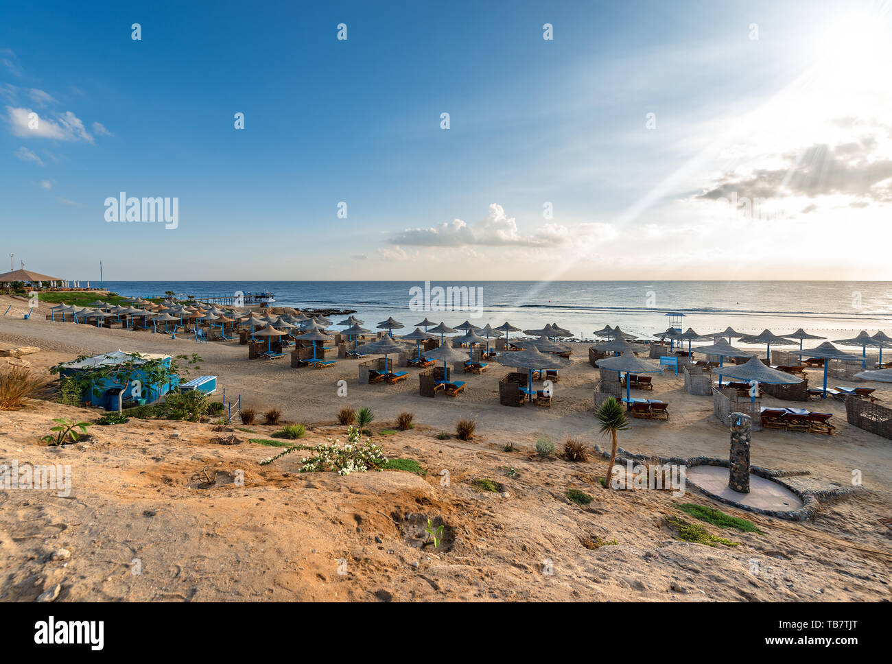 Das rote Meer in der Nähe von Marsa Alam, Ägypten, Afrika. Strand mit Liegestühlen und Sonnenschirmen. Im Hintergrund das Korallenriff und Marine Stockfoto