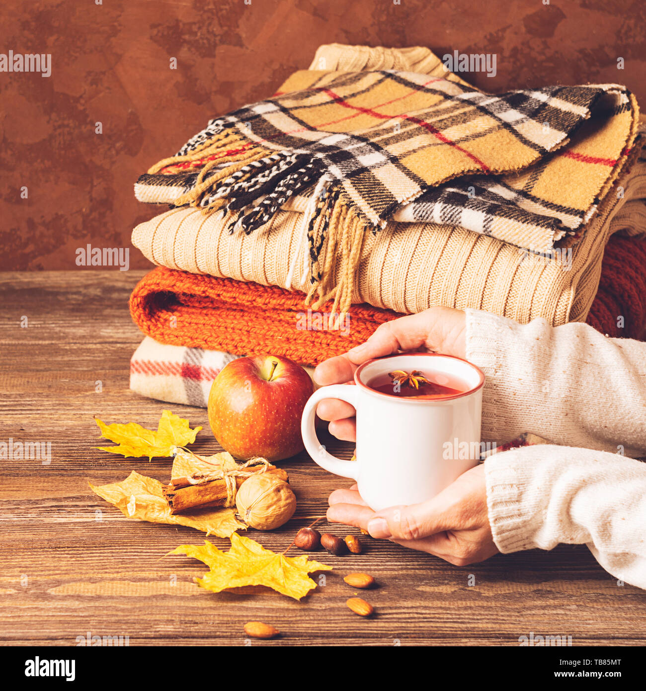 Eine Tasse heißen Getränk in weibliche Hände und ein Stapel aus Gewirken Kleider auf einem hölzernen Hintergrund. Herbst Konzept. Kopieren Sie Platz. Selektive konzentrieren. Quadratischen Rahmen Stockfoto