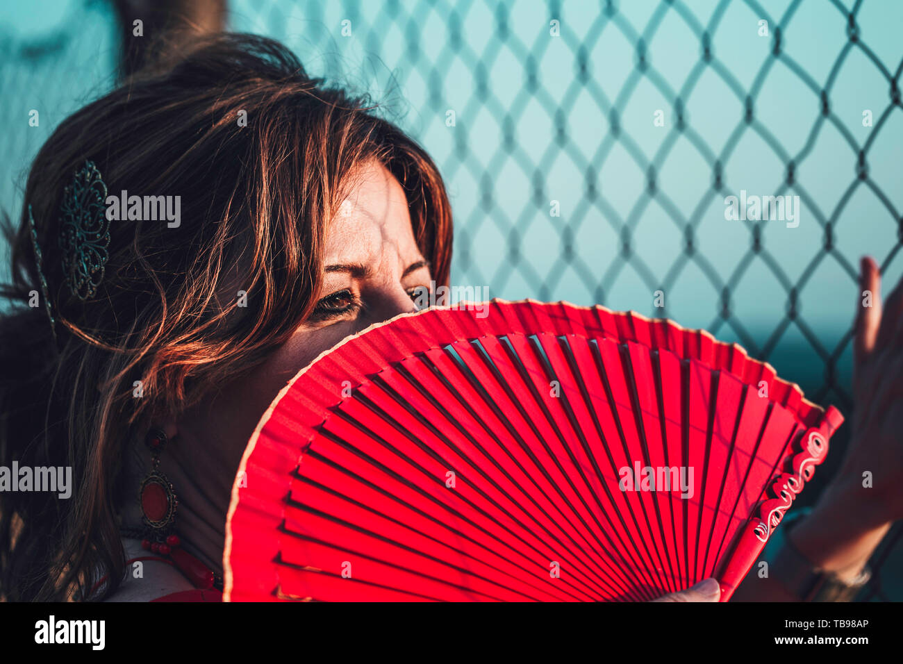 Nahaufnahme Porträt einer wunderschönen rothaarige Frau deckt die Hälfte der Fläche mit rotem Ventilator, Zaun und Schatten Stockfoto