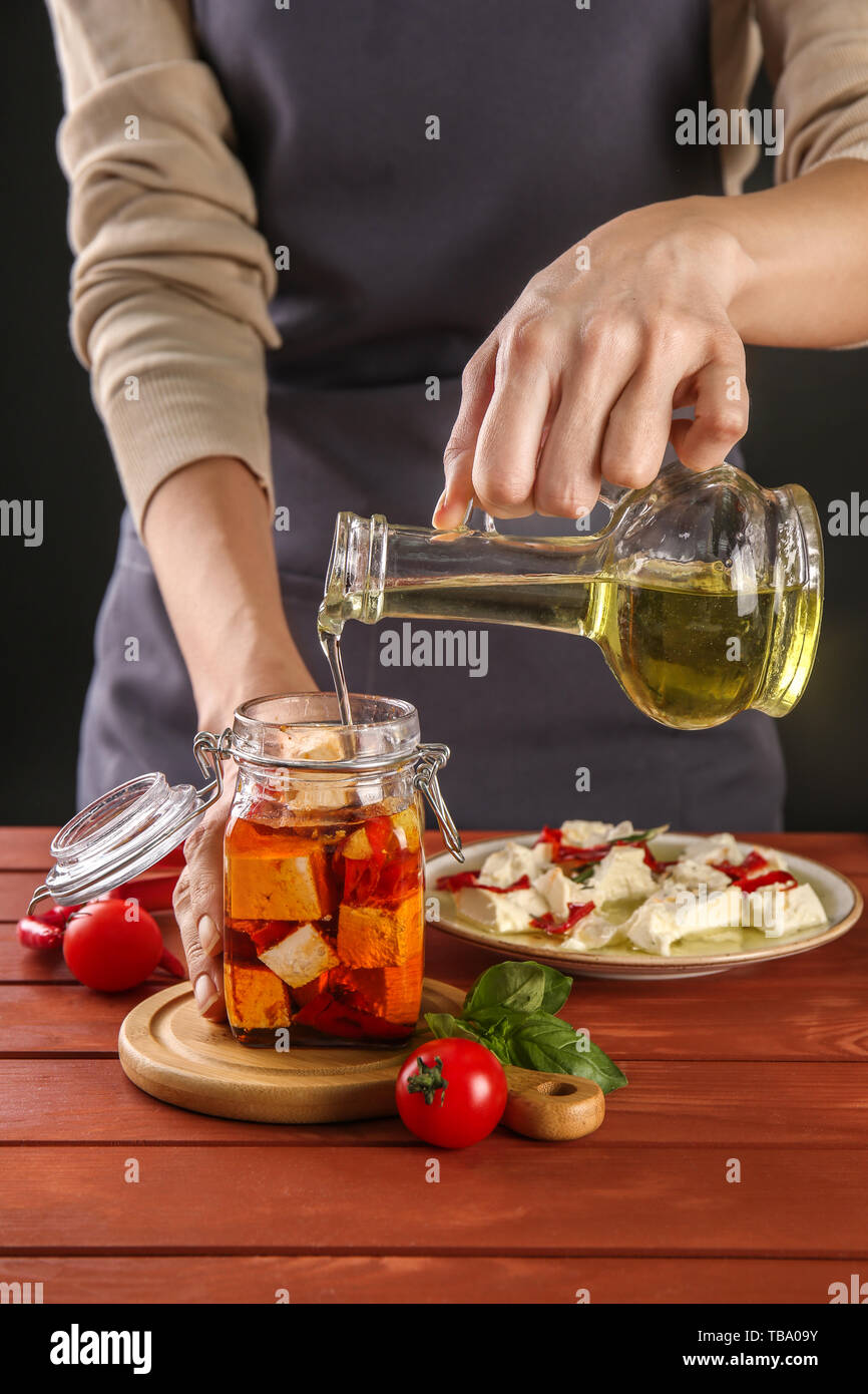 Frau gießen Olivenöl in Glas Glas mit lecker Feta Käse auf Tisch Stockfoto