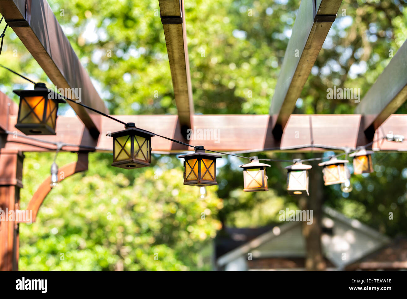 Nahaufnahme der Terrasse im Frühling Garten im Hinterhof des Hauses mit Laterne Lampen leuchten hängen von Pergola Vordach Pavillon aus Holz und Pflanzen Stockfoto