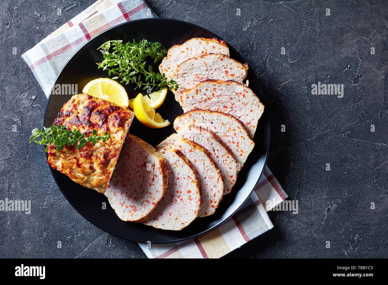 Huhn Terrine in Scheiben geschnitten serviert mit Zitronenscheiben und frischem Thymian auf einer schwarzen Platte auf einer konkreten Tabelle, Ansicht von oben, flatlay Stockfoto