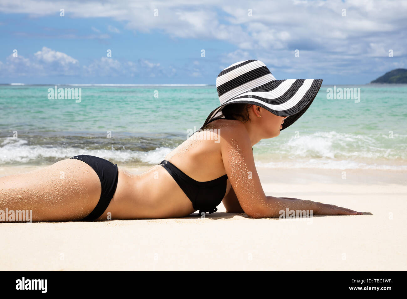 Seitenansicht einer jungen Frau im Bikini tragen Gestreifte Hut Liegen am Strand Stockfoto