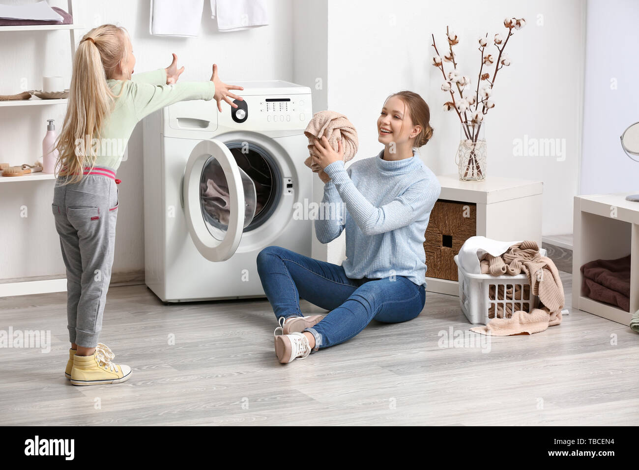 Junge Frau und ihre kleine Tochter spielen, während Wäsche zu Hause Stockfoto
