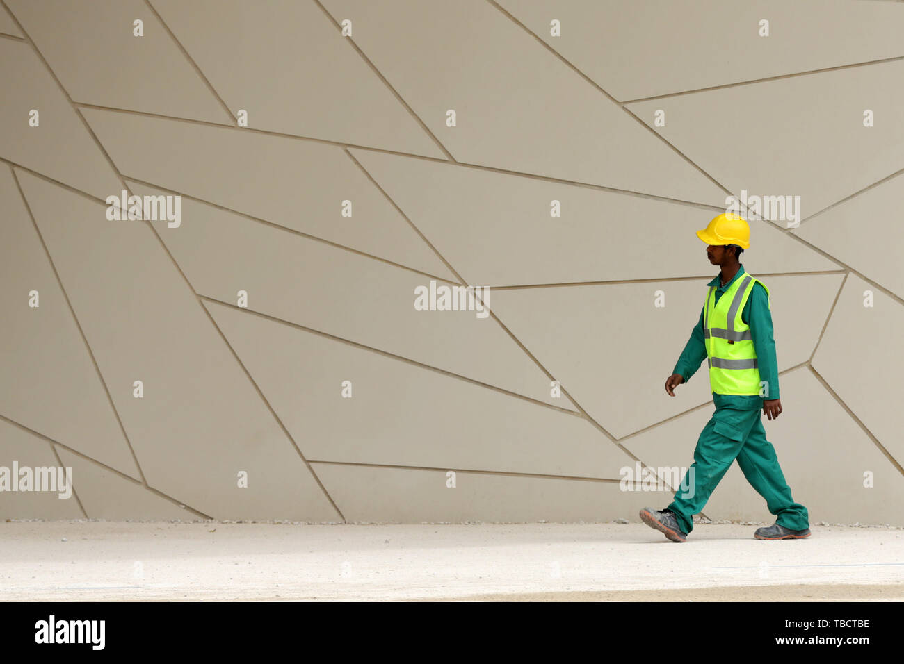 Doha, Katar - 11 April, 2019: Ein Arbeiter mit einer Berufsbekleidung und eine einheitliche Spaziergänge rund um die National Museum von Qatar. Stockfoto