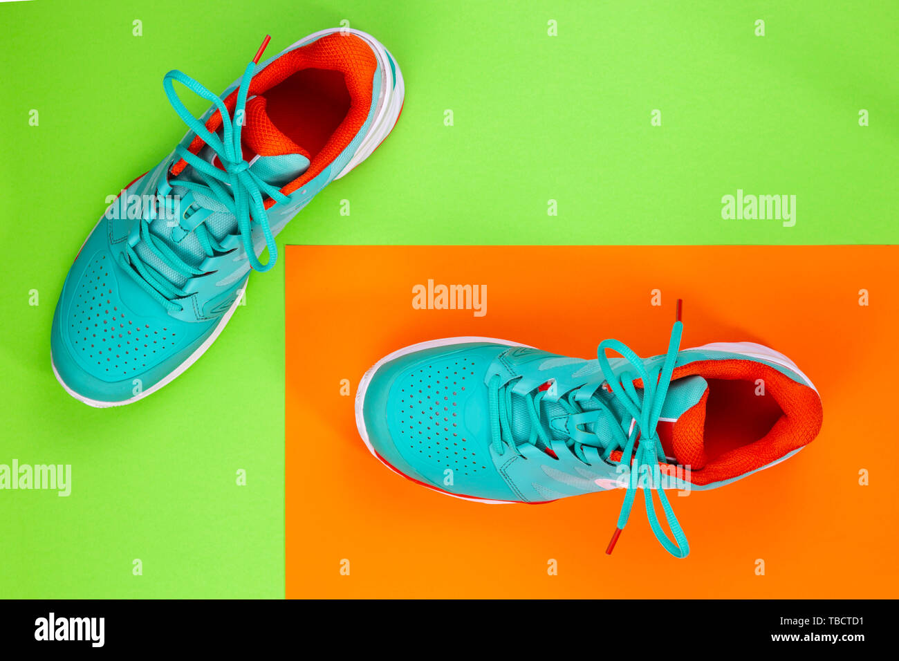 Rot, hellblau, weiß, Paar neue Tennisschuhe im Studio Schuß über grün, orange Hintergrund. Direkt von oben. Stockfoto