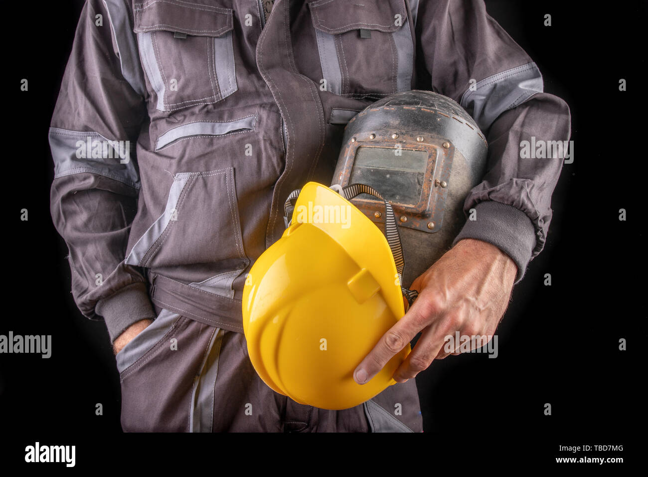 Ein Arbeiter in Arbeitskleidung mit einem schweissverfahren Maske in der Hand. Spezielle Berufskleidung für Mitarbeiter. Der dunkle Hintergrund. Stockfoto