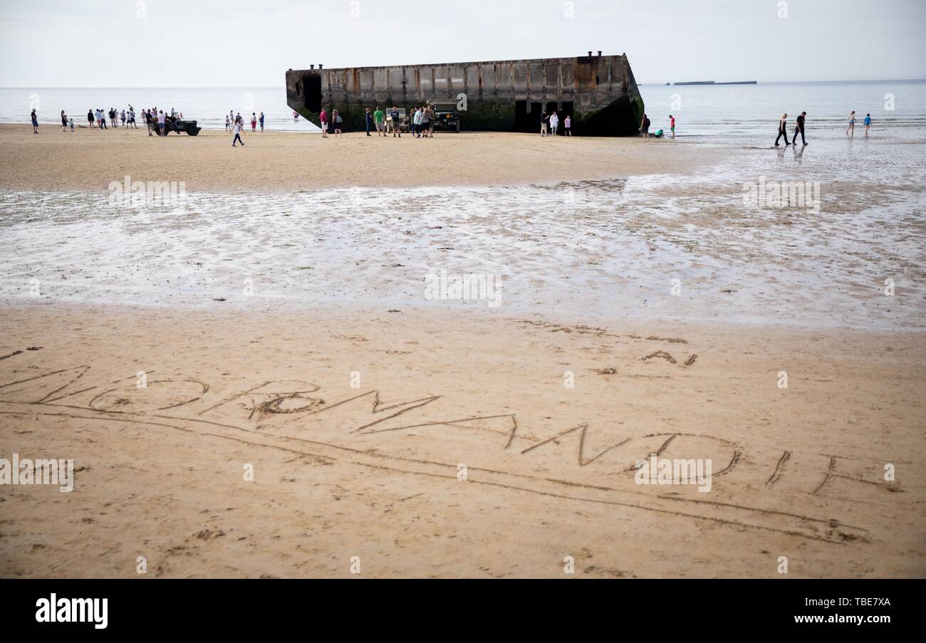 Frankreich. 01. Juni 2019, France (Frankreich), Arromanches-Les-Bains: Überreste des ehemaligen Hafen sind bei Gold Strand entfernt, hinter dem Schreiben "Normandie", die in den Sand geschrieben wurde. Nach der Landung der alliierten Truppen im Zweiten Weltkrieg, einer der zwei künstliche Häfen (Mulberry B) gebaut wurde an der Küste von Arromanches-les-Bains, durch die Truppen und liefert an Land gebracht wurden. 06.06.2019 ist der 75. Jahrestag der Landung der alliierten Truppen in der Normandie (D-Day). Foto: Kay Nietfeld/dpa Stockfoto