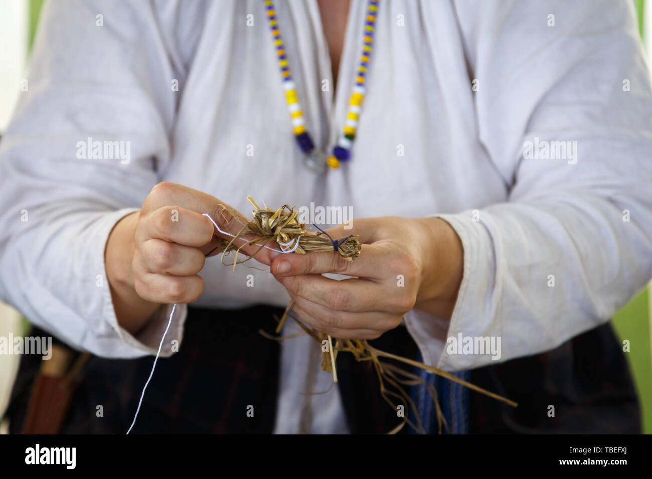 Frau in einem weißen Hemd mit Perlen zeigt, wie Sie einen Stroh Spielzeug machen Stockfoto