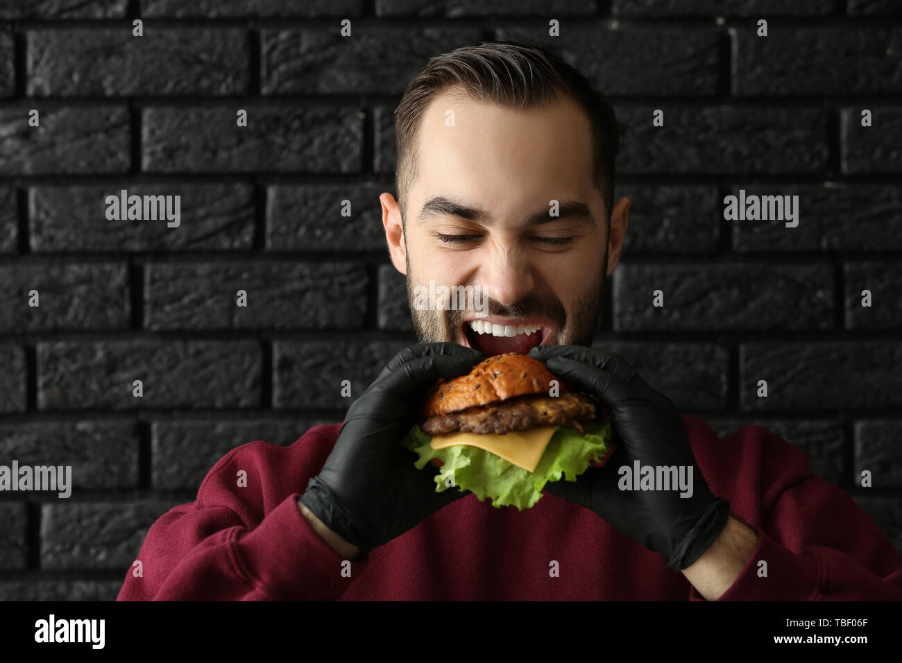 Mann essen leckere Burger auf dunklem Hintergrund Stockfoto