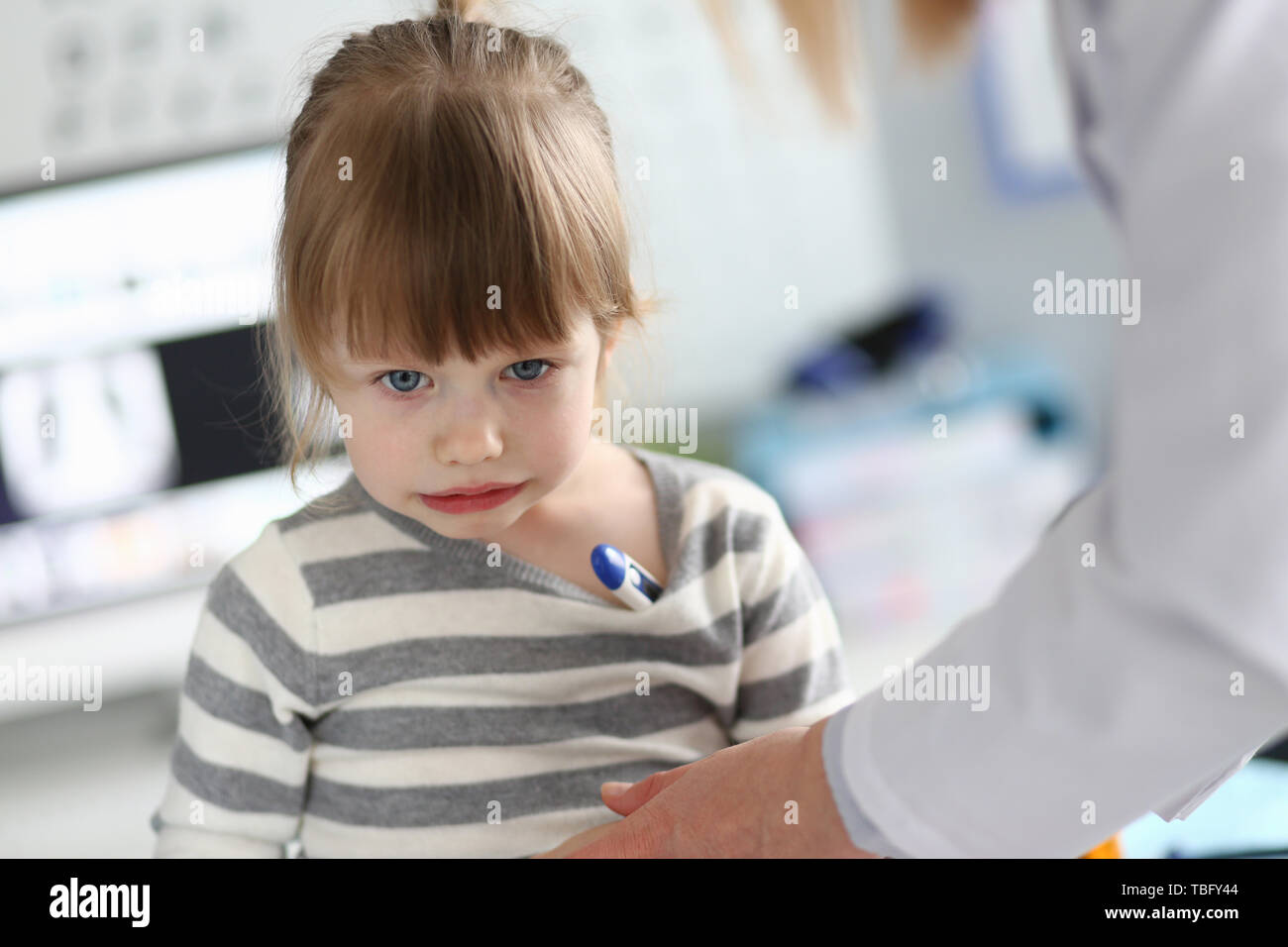 Süße nachdenkliche kleine Mädchen mit Thermometer unter ihre achsel Stockfoto