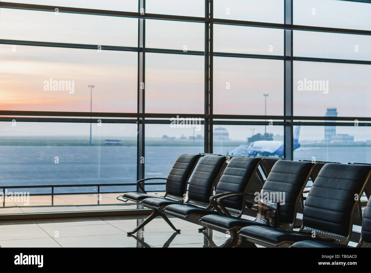 Blick auf Flughafen, interoir leeren Bank Stühle in der Abflughalle bei Sonnenaufgang. Flugzeug und Gebäude im Hintergrund. Reise und Verkehr Konzept Stockfoto