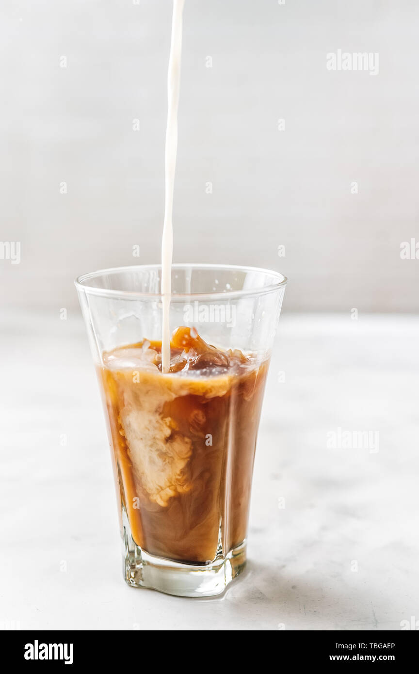 Eiskaffee mit Gießen Milch in Glas auf weißem Hintergrund Stockfoto