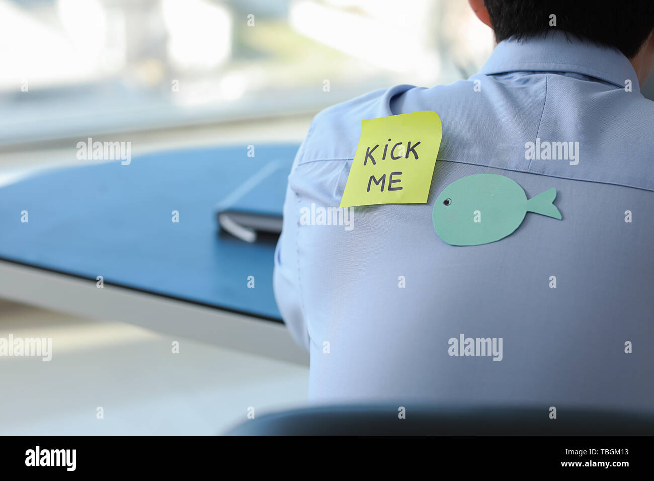 Haftnotiz mit Text tritt mich und Papier Fisch auf der Rückseite der Mann bei der Arbeit im Büro. April Fools' Day prank Stockfoto