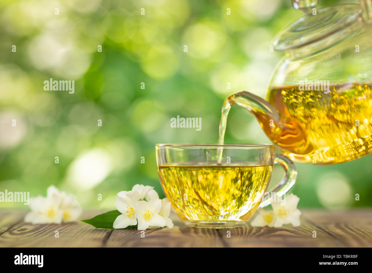 Pflanzliche Jasmin Tee Gießen der Teekanne aus Glas in Schale auf Holztisch  mit unscharfen grün Natur Hintergrund Stockfotografie - Alamy