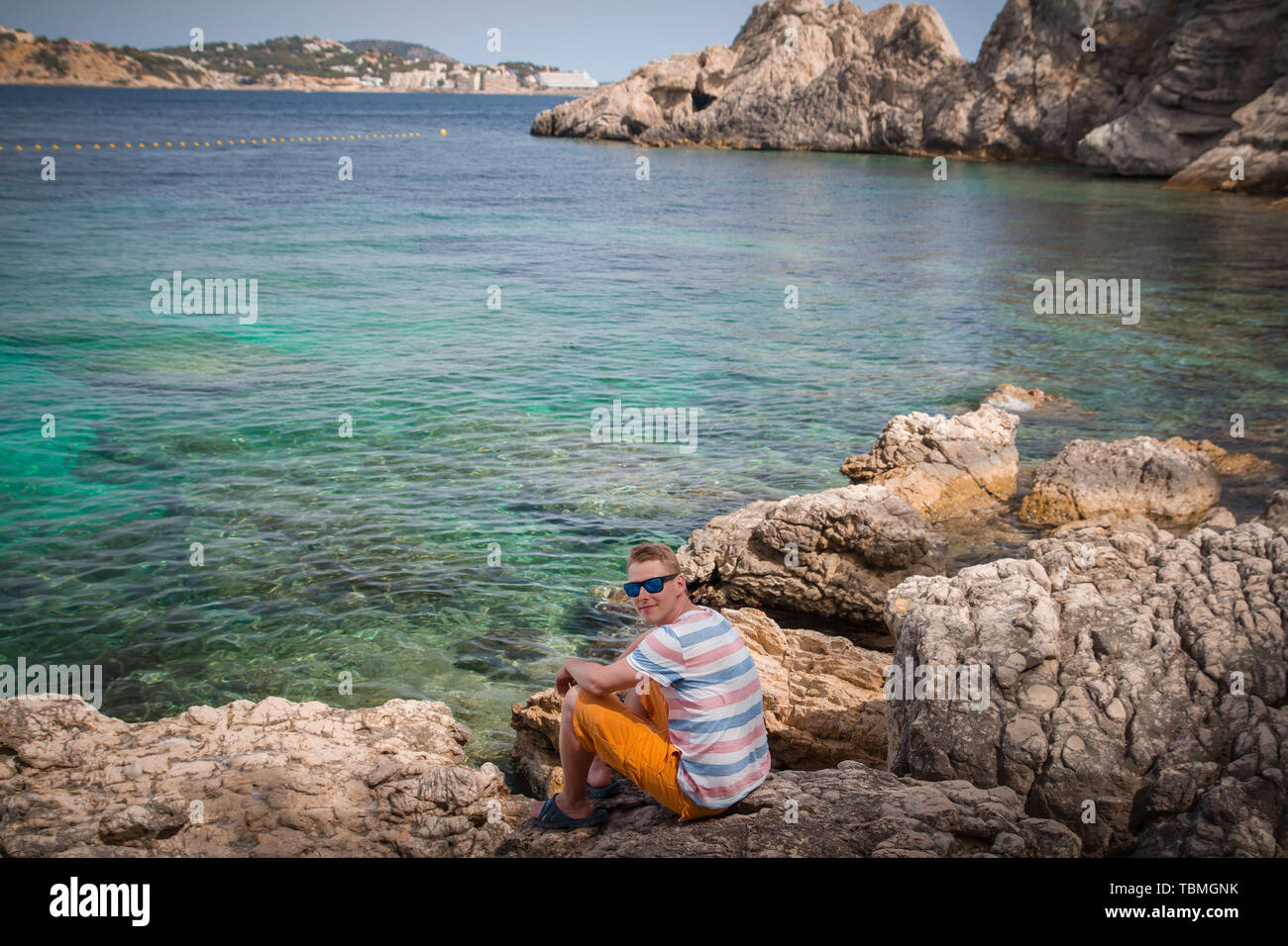 Kaukasische Mann mit Sonnenbrille und t-shirt sitzen auf den Felsen am Meer Stockfoto