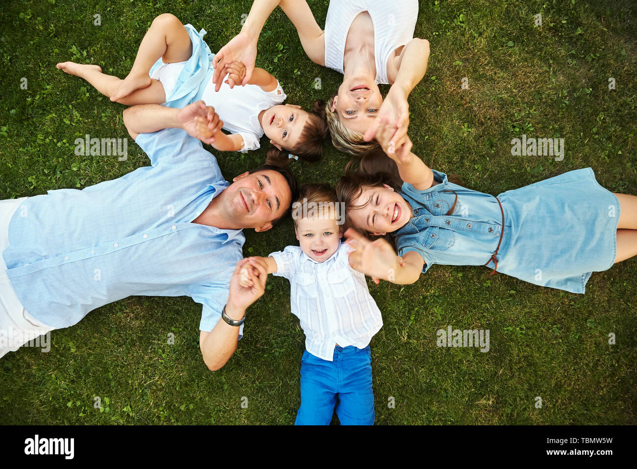 Gerne verspielt Familie, die auf dem Gras im Freien. die Eltern mit den Kindern im Sommer. Mama, Papa und Kinder Stockfoto
