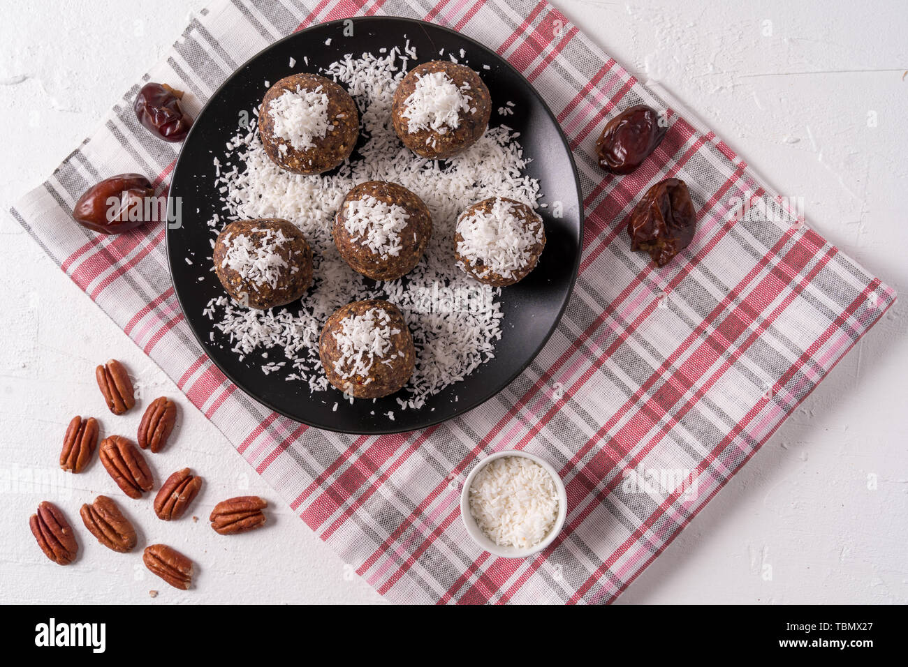 Gesunde bio Energie Kugeln mit Datteln, Backpflaumen, Rosinen, Erdnüsse, mit Kokos Späne, in schwarz auf weißem Hintergrund, flach. Stockfoto