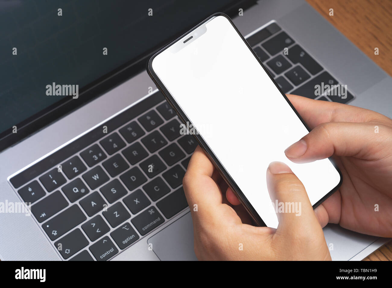 Mann mit Smartphone über das Laptop mit leerer Bildschirm. Technologie Werbung Konzept. Stockfoto