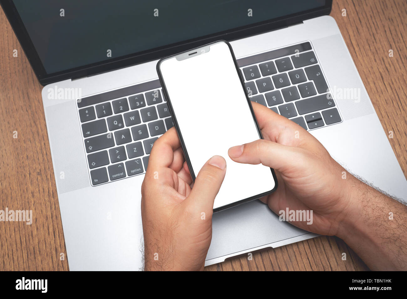 Mann mit Smartphone über das Laptop mit leerer Bildschirm. Technologie Werbung Konzept. Stockfoto