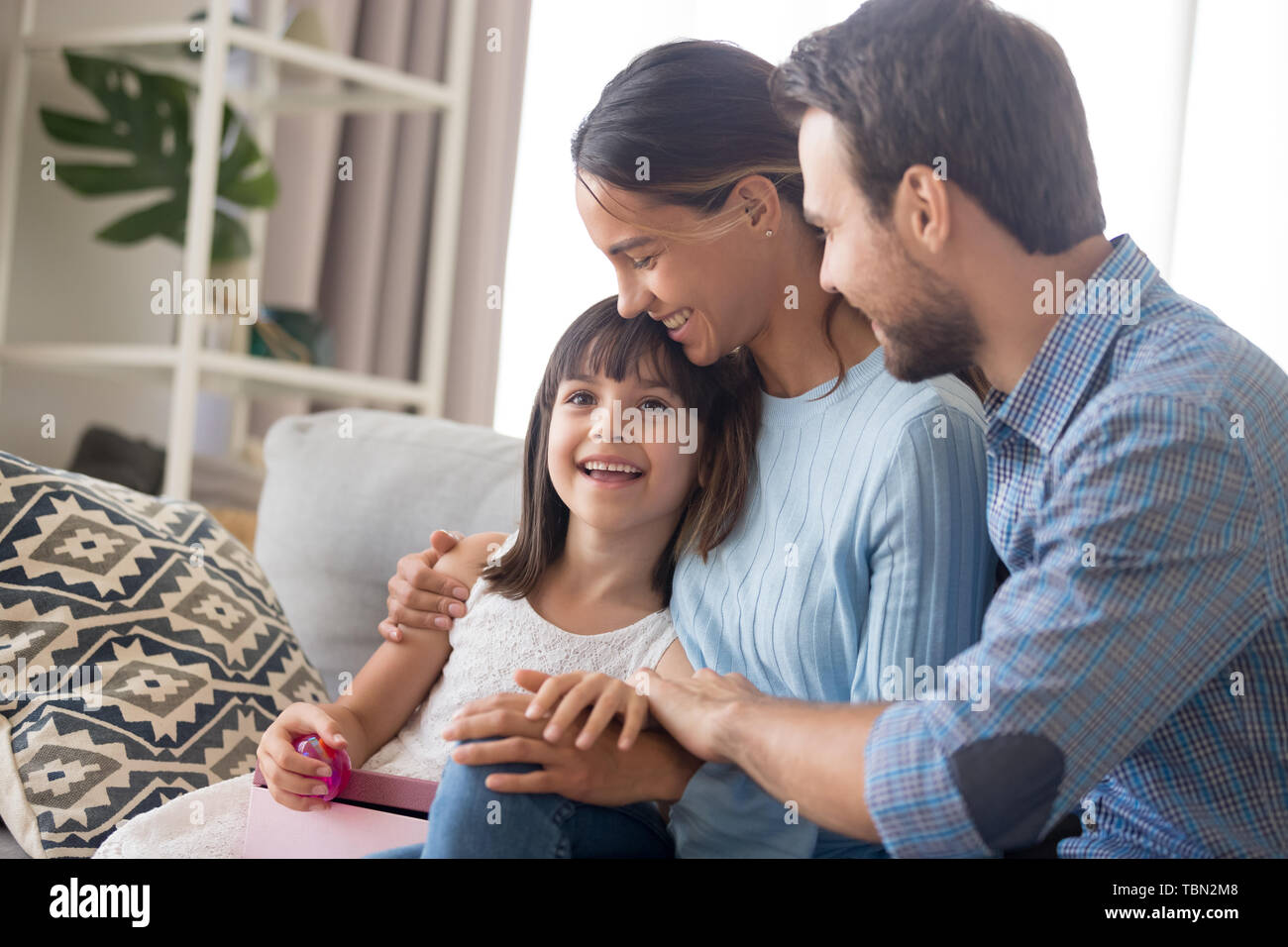 Glückliche Familie mit Kind auf der Couch kuscheln mit Geburtstag gratulieren. Stockfoto