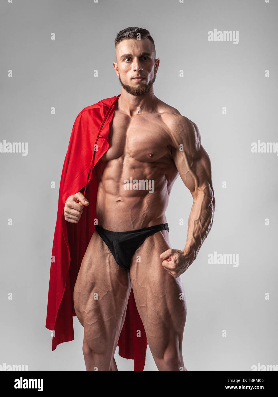 Männlichen Bodybuilder setzt auf seinen Schultern, einen roten Mantel mit einem ernsten Gesicht Stockfoto