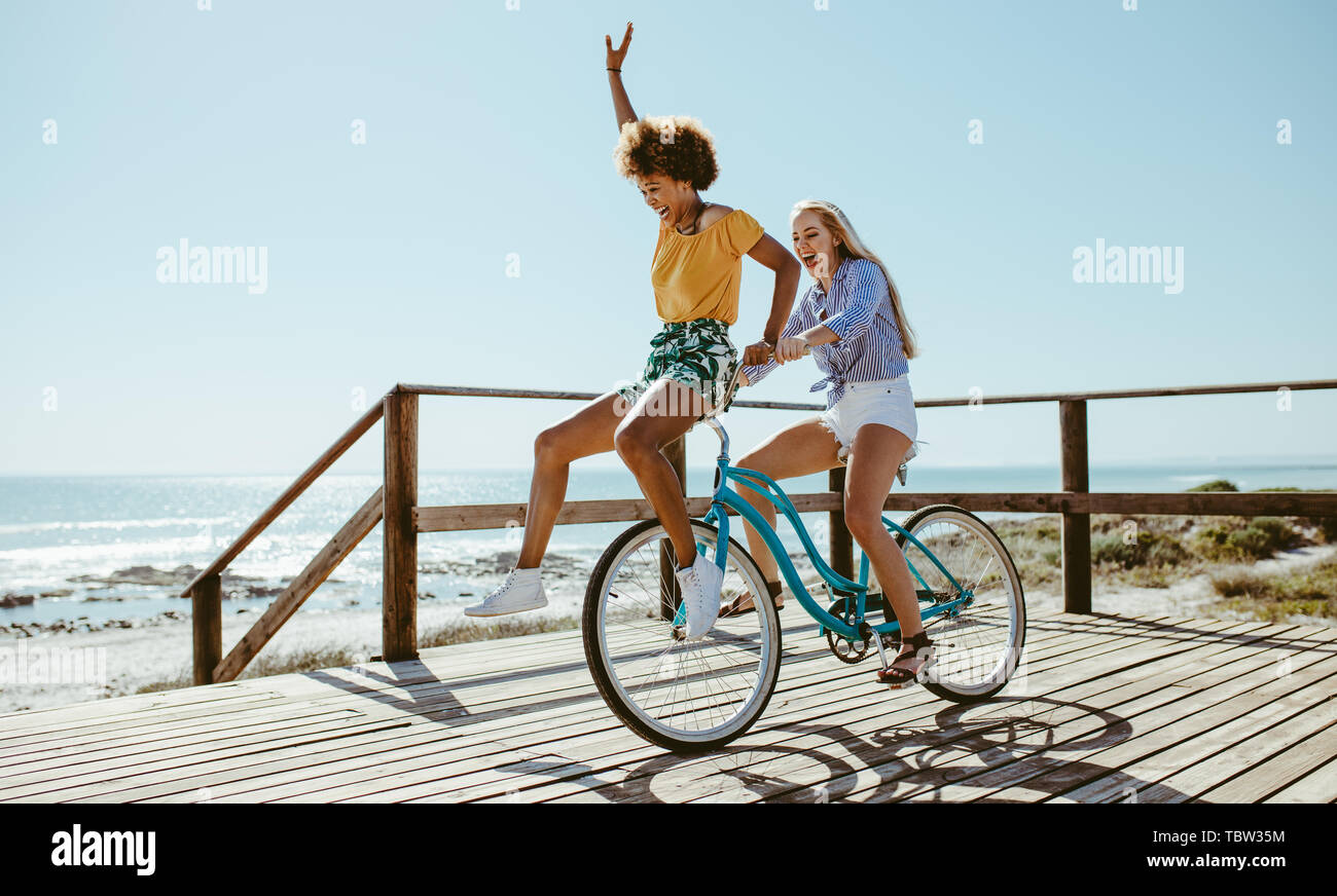 Fröhlicher junger Frauen eine Radtour zusammen am Strand. Weibliche Freunde Spaß auf ein Fahrrad an der Promenade am Meer. Stockfoto