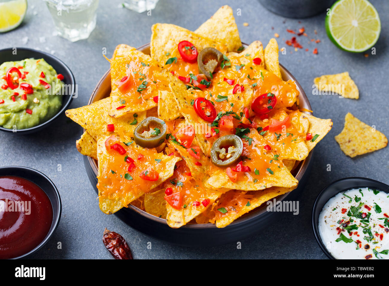 Nachos Chips mit geschmolzenem Käse und Dips Vielfalt in schwarz Schüssel. Grauen Stein Hintergrund. Stockfoto