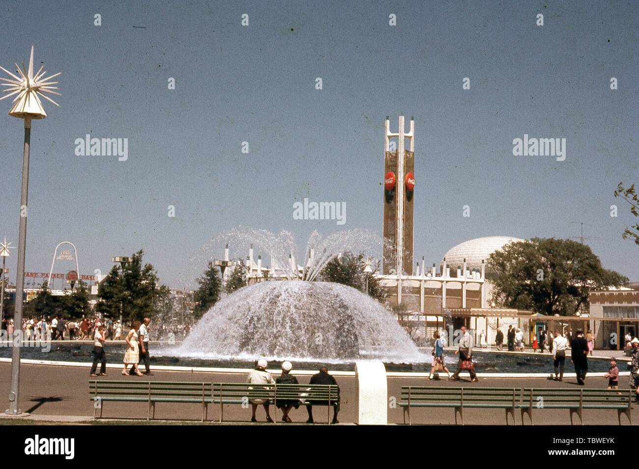 Messebesucher, an einem sonnigen Tag, gehen und sitzen durch einen Brunnen in der Nähe der Coca Cola Pavillon, 1964 in New York World's Fair, Flushing Meadows Park, Queens, New York, Juni, 1964. () Stockfoto